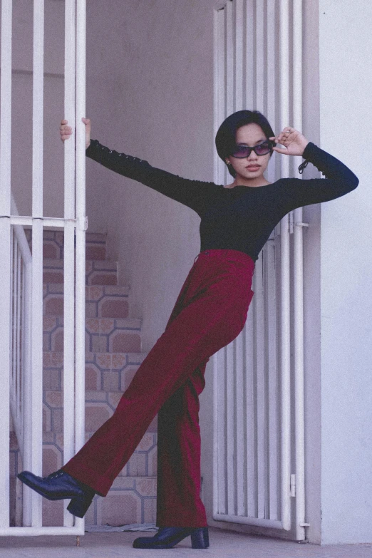 woman posing in front of large doors wearing sunglasses and long pants