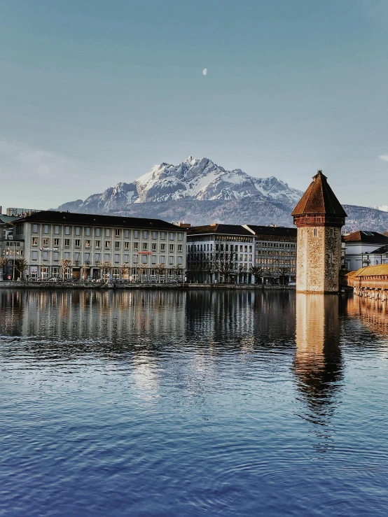 the water is clear and very calm, with buildings near the mountain