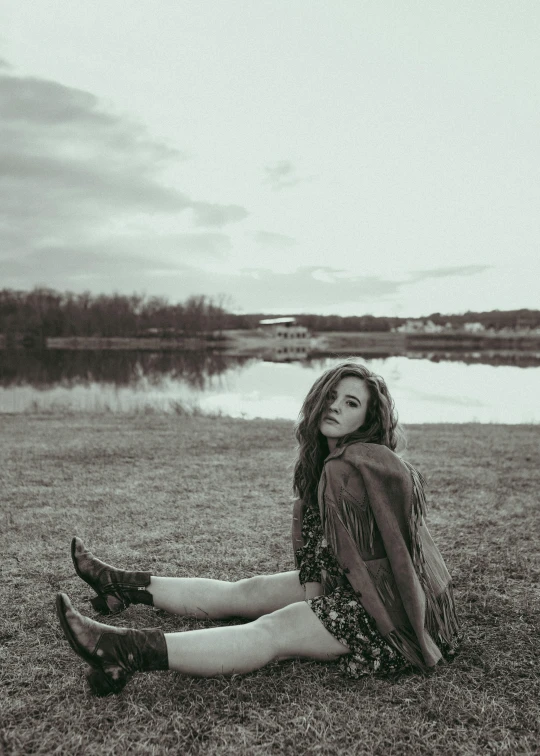 a woman sitting by the water with her feet on the ground