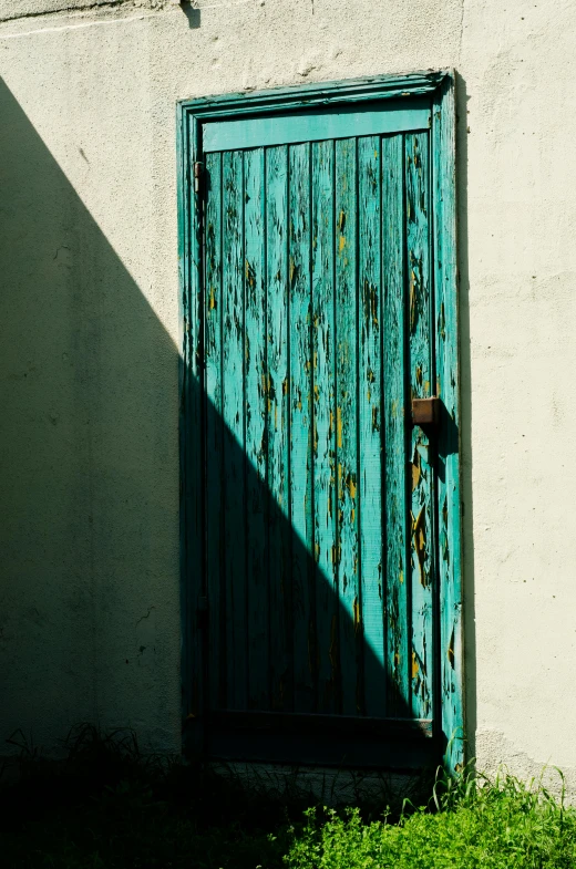 an old door is painted turquoise, casting a shadow on the wall