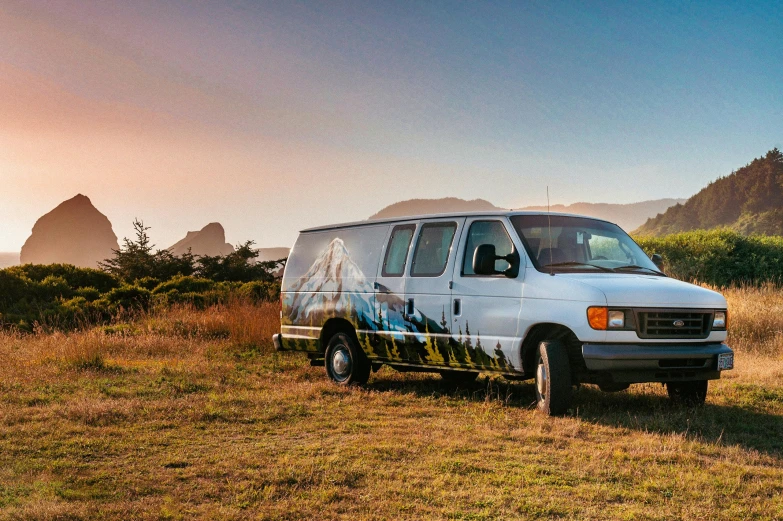 a van with a painting of mountains and trees is parked on a hill