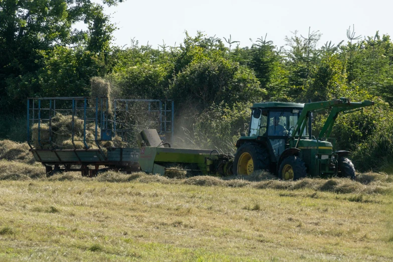 tractor being pulled by trailer loaded with bales of hay