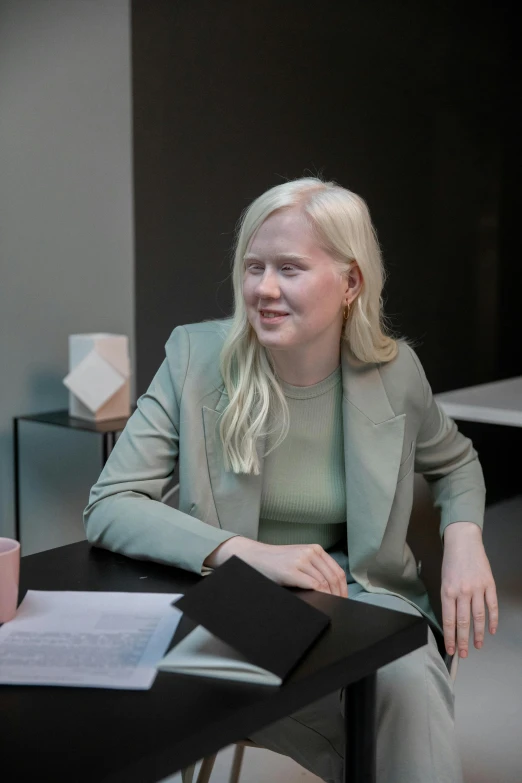 a blonde woman sitting down on the edge of a desk