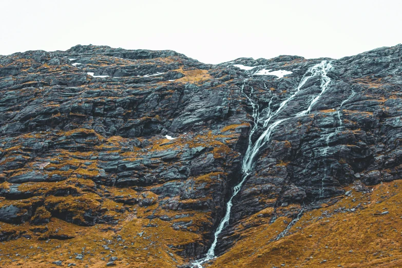 a waterfall near a mountain side by side