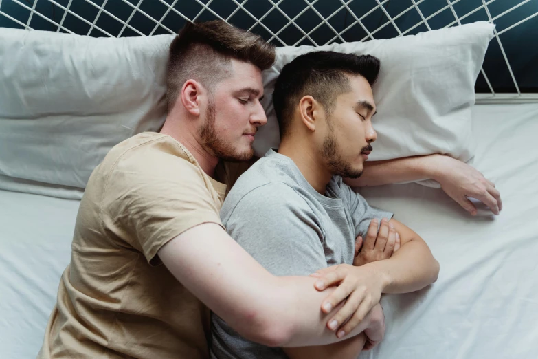 two men who are looking at each other while laying in bed