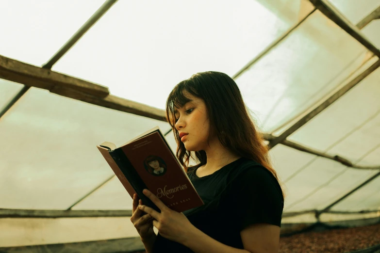 a woman holding up her book while in a greenhouse