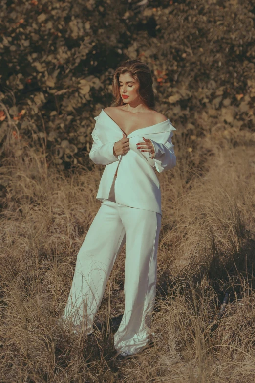 a woman in white with one sleeve down standing on grass