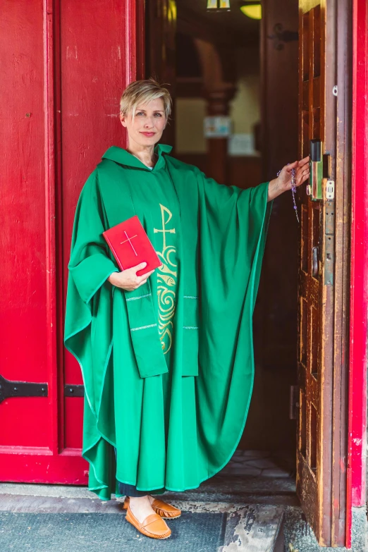 woman in green priest robe standing in front of the red door