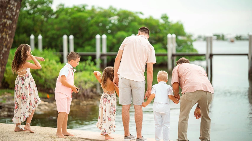 a family with three small s standing on the dock by the water