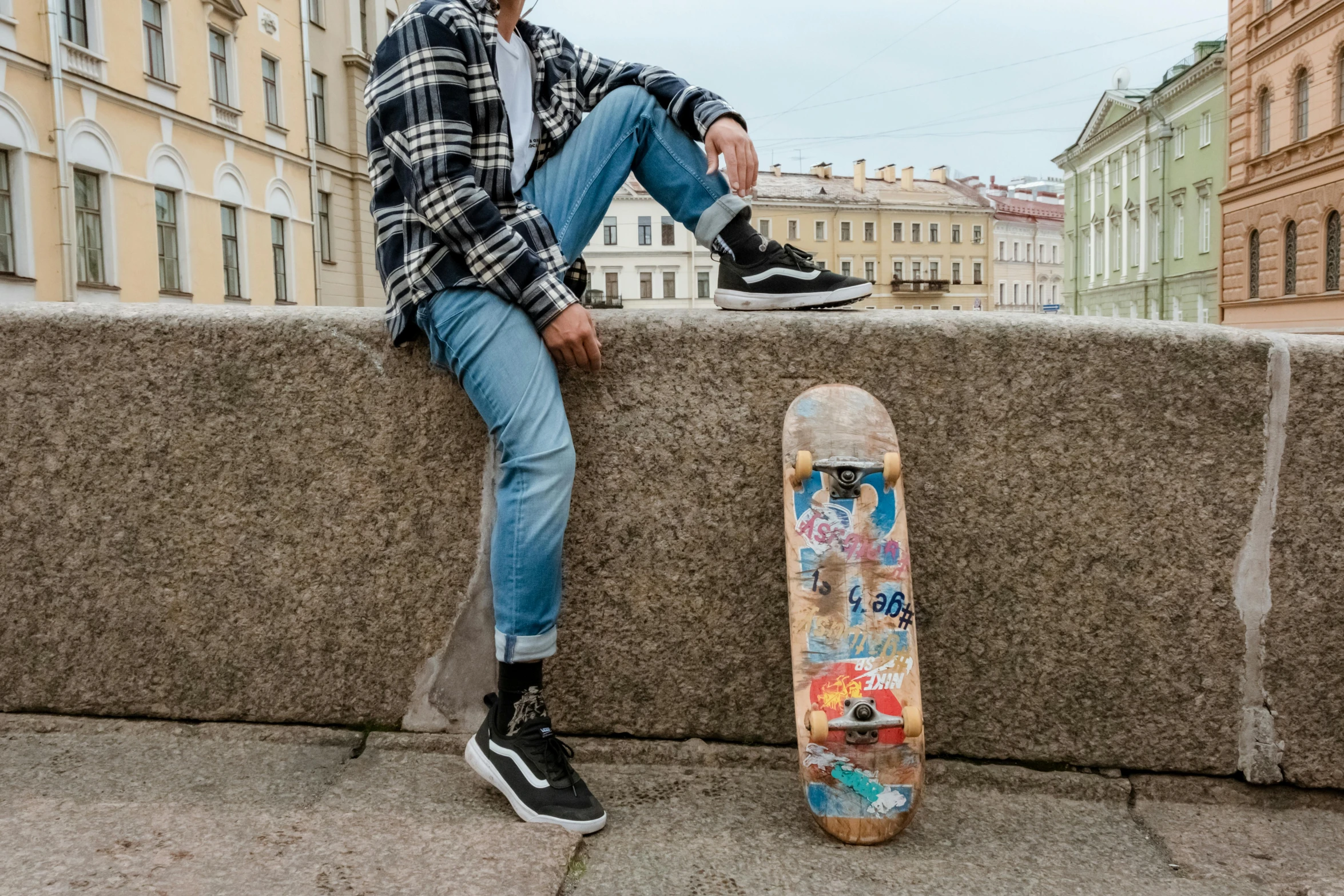 a young man sitting on a ledge next to a skateboard