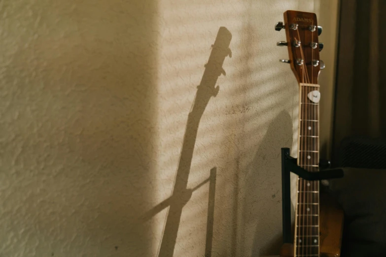 a guitar resting in a corner by a window