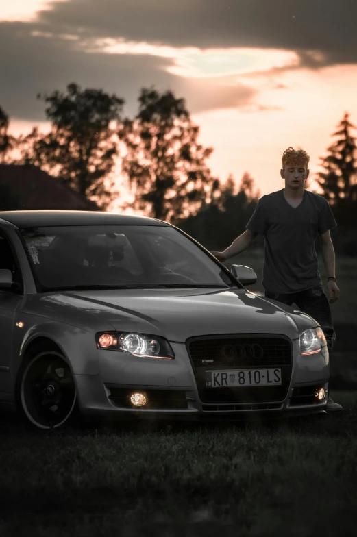 a man leaning on a parked car on the grass