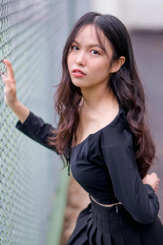 a woman in a black dress stands next to a wire fence