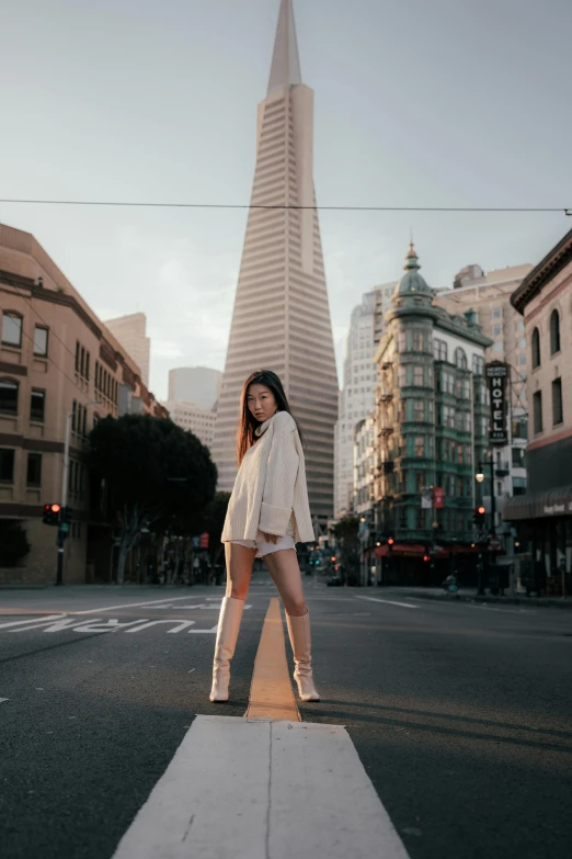 a woman in boots and a coat posing for a po in the middle of an intersection