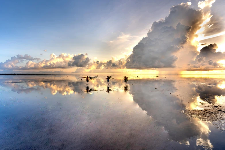 three people standing in the water watching a very colorful cloud looms over