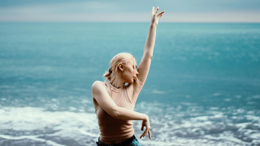 a young blond woman in a beige top reaches up to catch a ball