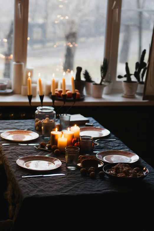 a table with plates and candles with a window and large open window in the background