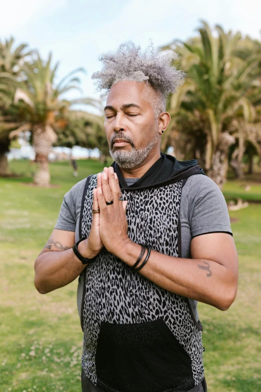 a man with grey hair and wearing a vest holding his hands together