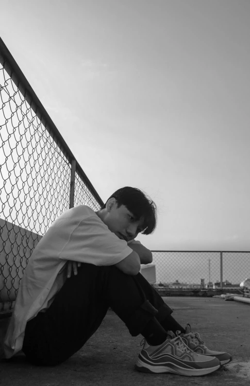 a man with his head down sitting in front of a fence