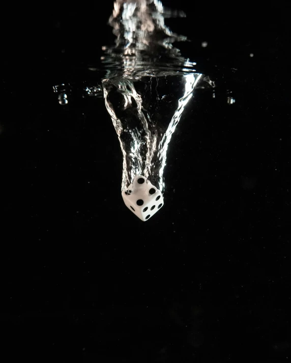a dice floating inside of water with dark background