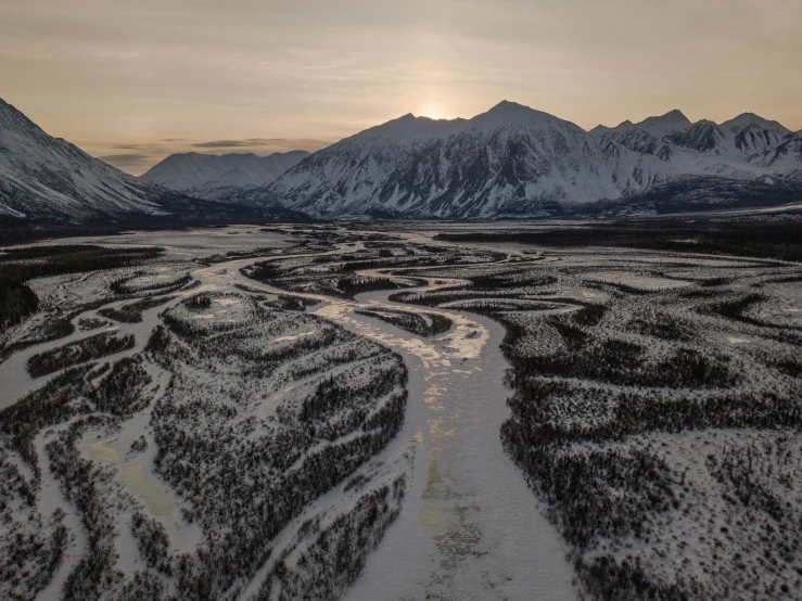 a snowy landscape at sunset with a river meanders through it