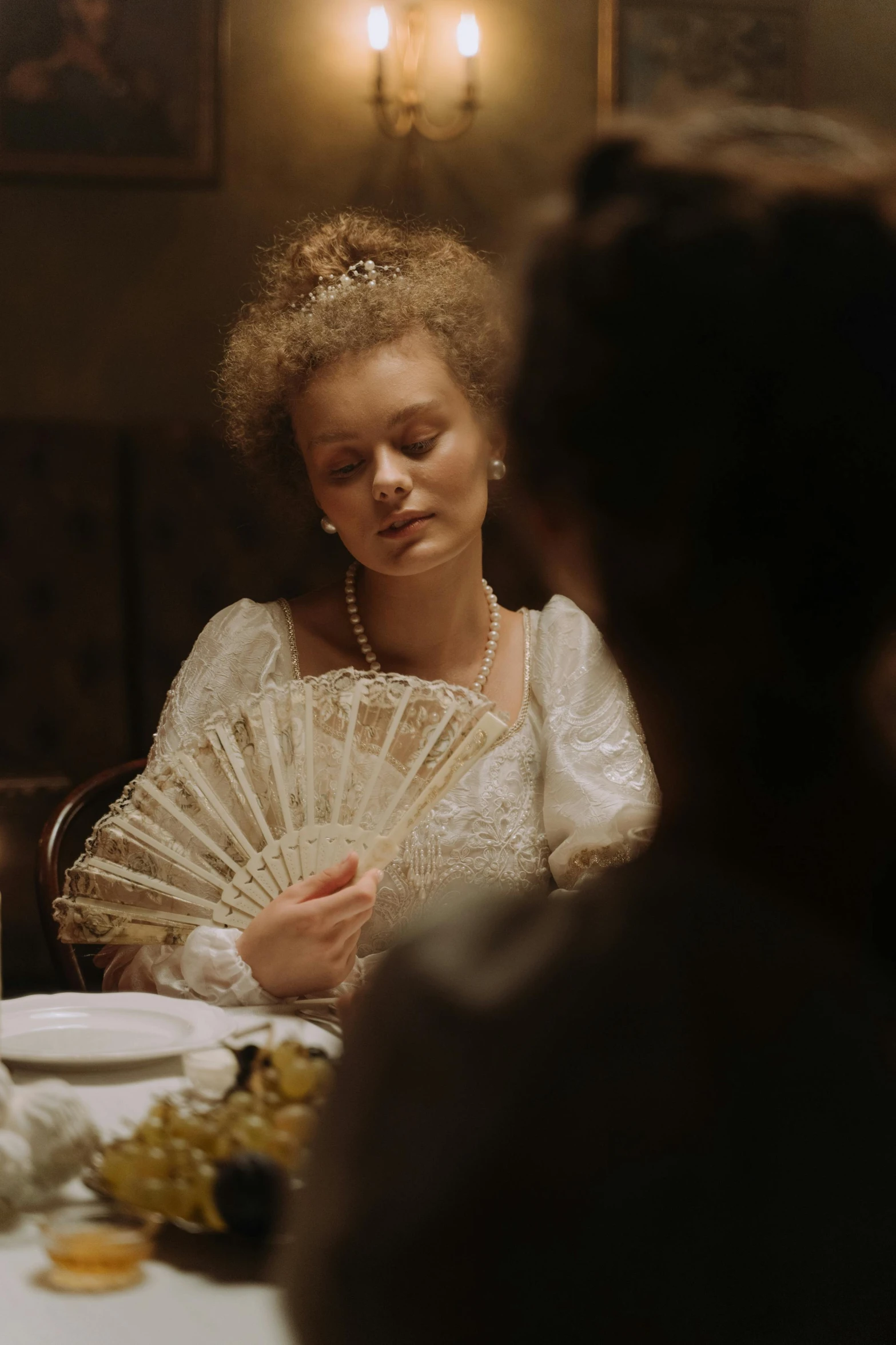 woman holding up an open - air fan in a fancy dinner setting