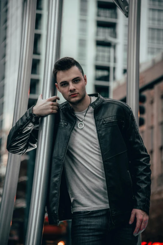 man in grey shirt leaning against a metal pole