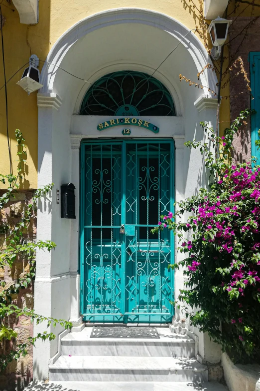 a green door is on a yellow building with purple flowers and shrubbery