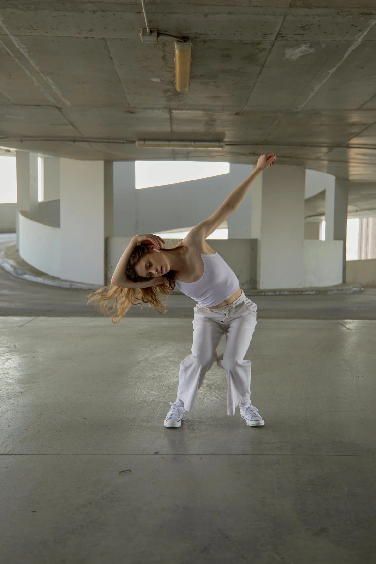 a woman wearing all white is dancing in the middle of an empty parking garage