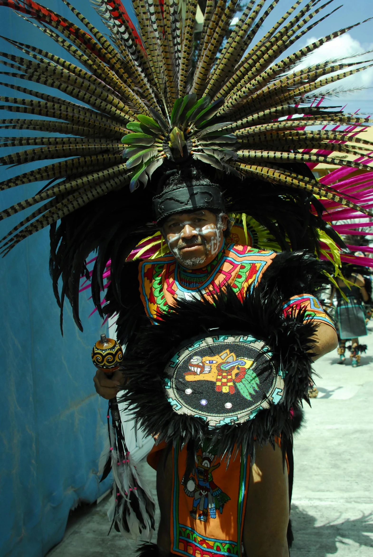 man dressed in colorful costume walking with a large feather headpiece