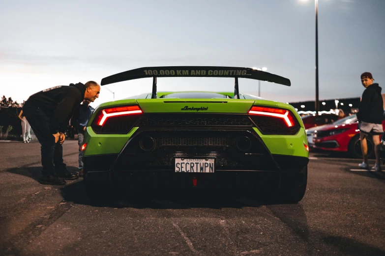 a lamb - looking car is parked in a lot with people standing around