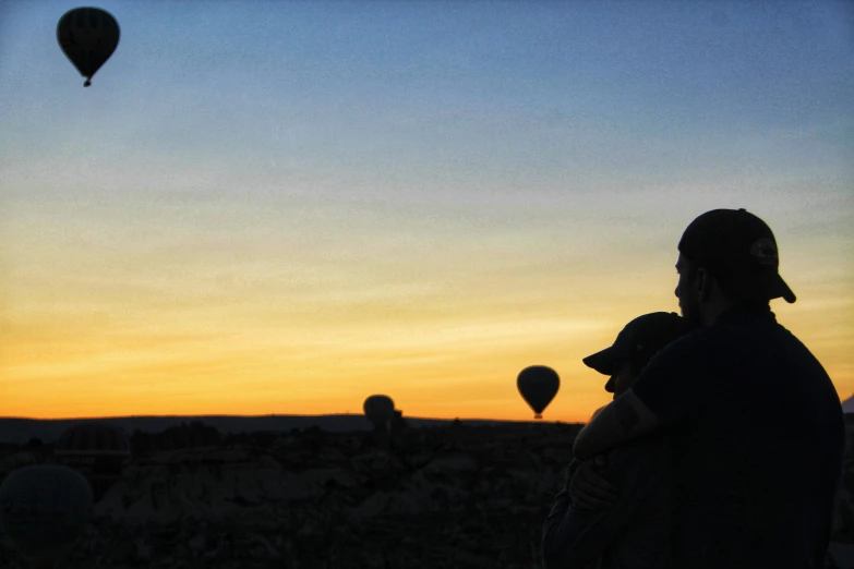 a man holding a child watching some  air balloons