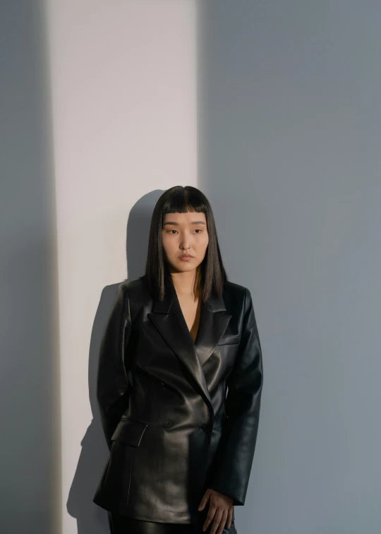 a woman in black leather jacket leaning against a wall