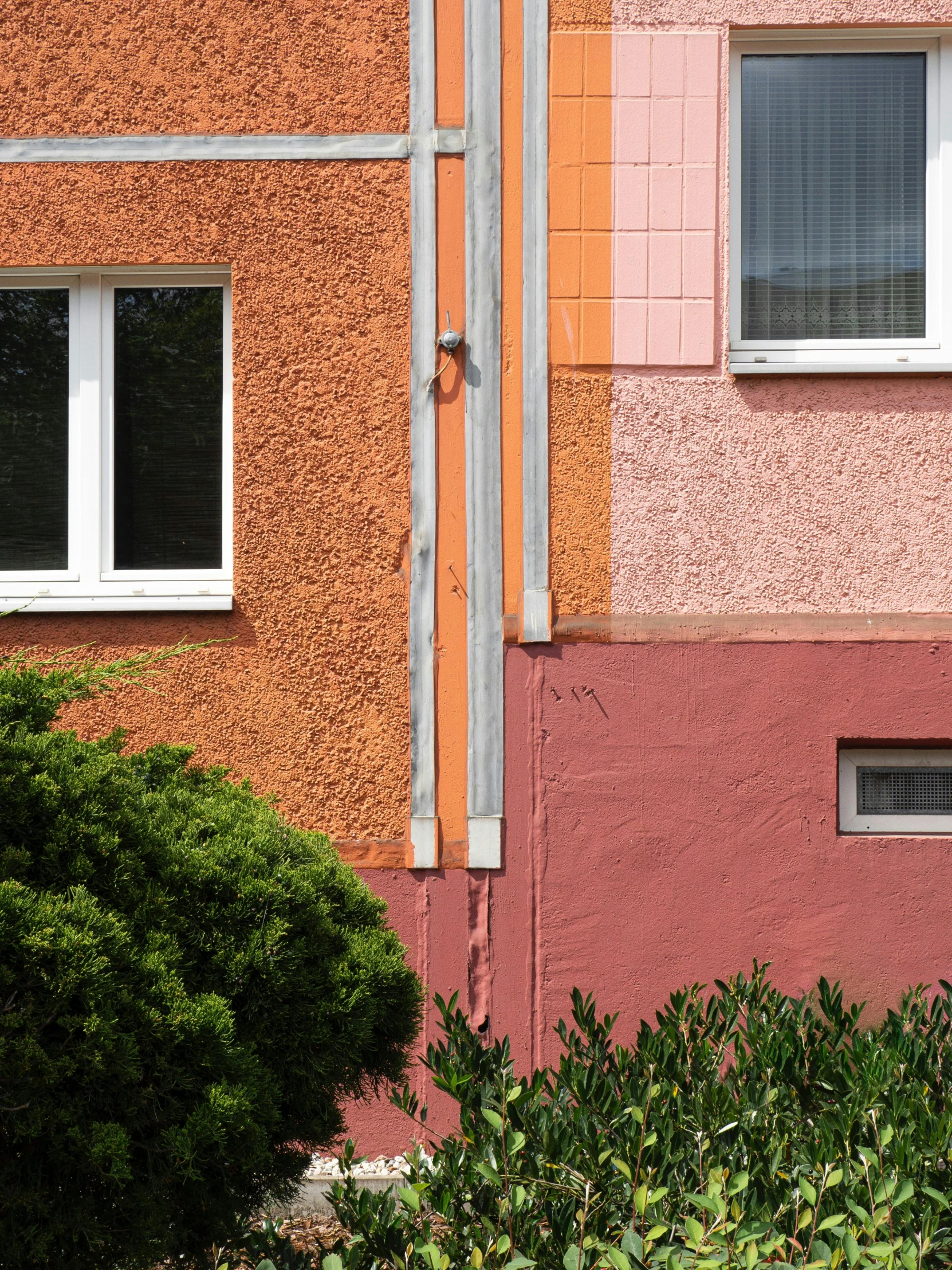 a side of a pink, orange and red building with three windows