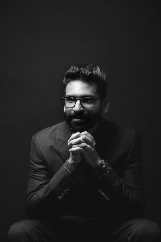 a man in black with glasses and a beard wearing a suit