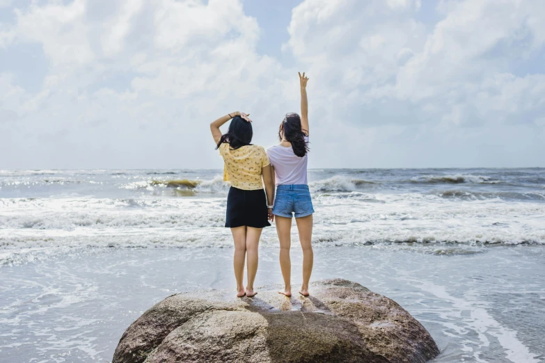 two women standing on rocks in front of the ocean