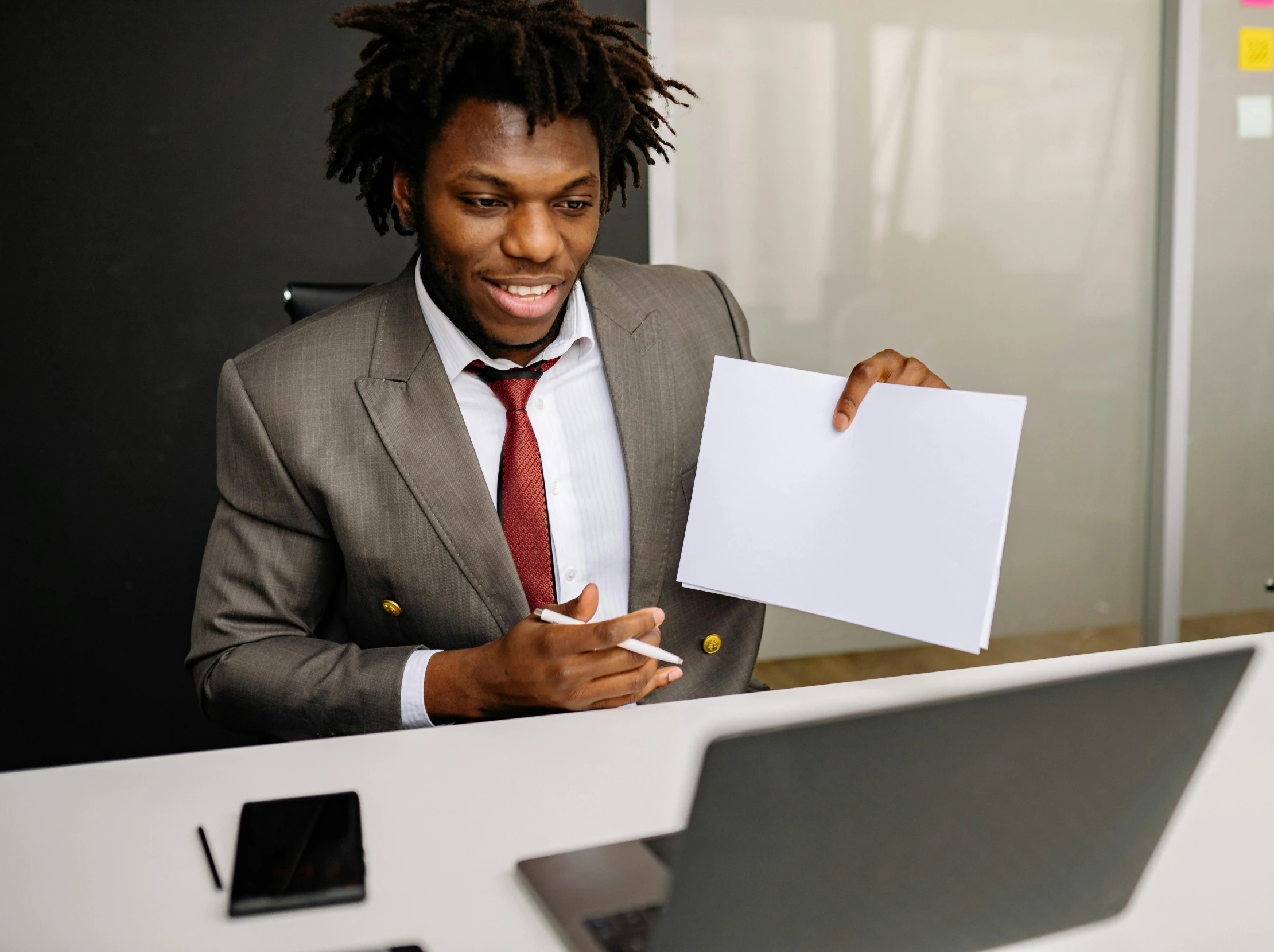 a man in suit holds papers at his desk