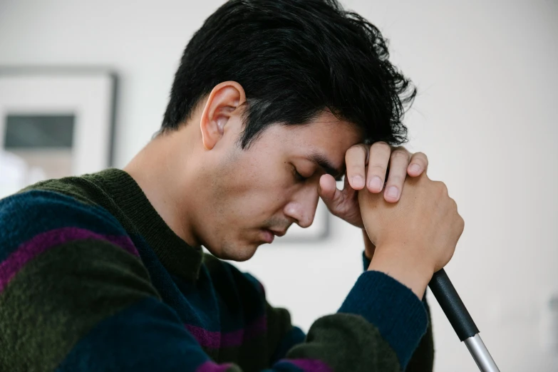 man in a sweater holds his head to his hands