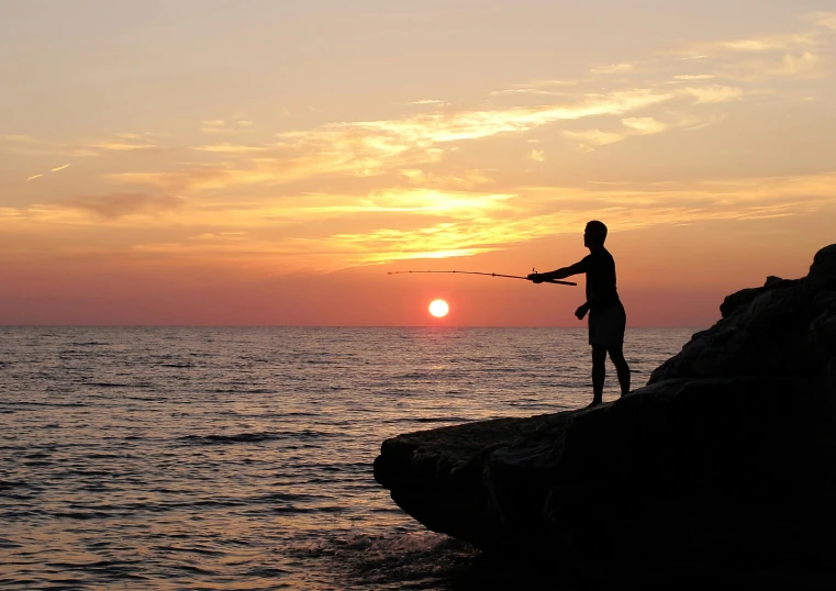 a person fishing from the shore at sunset