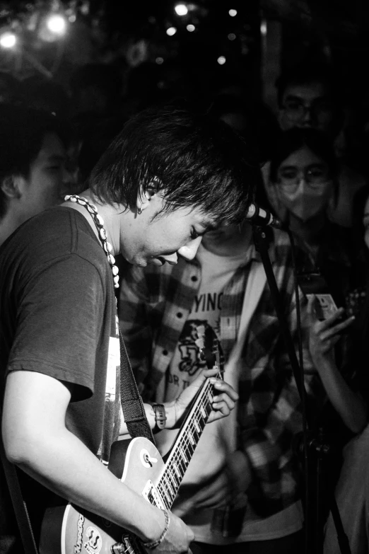a black and white po of a young man playing guitar in front of a microphone