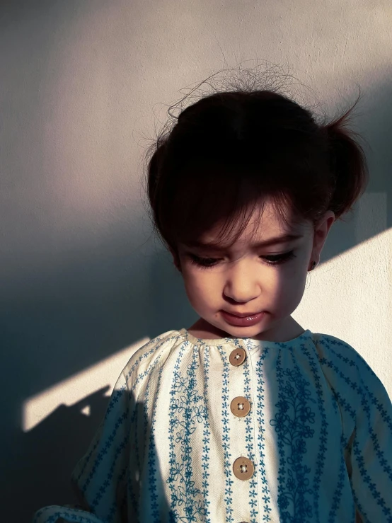 small child in striped blouse standing against wall