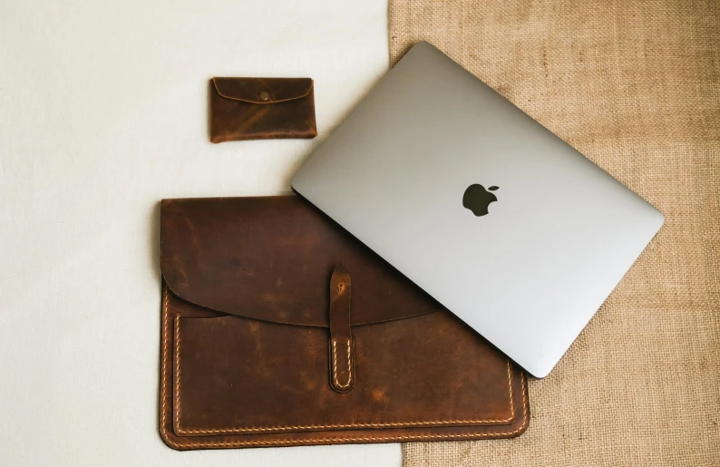 a macbook, wallet and sleeve on a white sheet