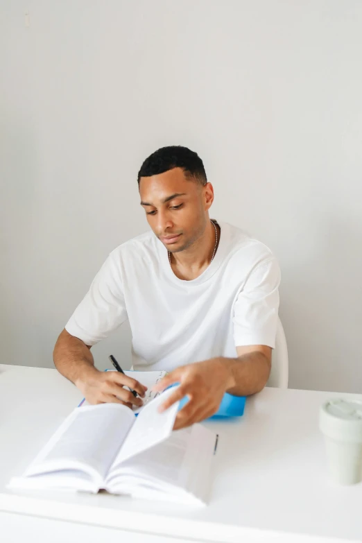 a young man sitting at a table while looking through a book