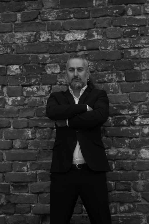 a man standing by a brick wall with his arms crossed