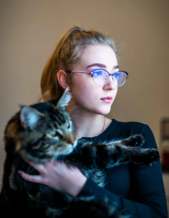 a girl with glasses holding a cat and a drink