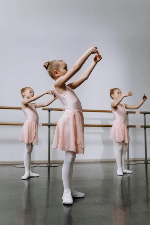 several girls in ballet dresses and tutus stand in front of a mirror