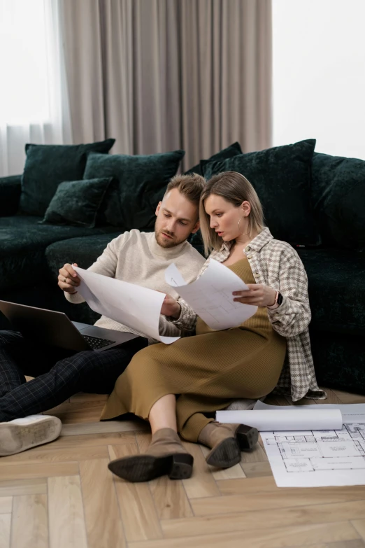 the man and woman are sitting on the floor looking at papers