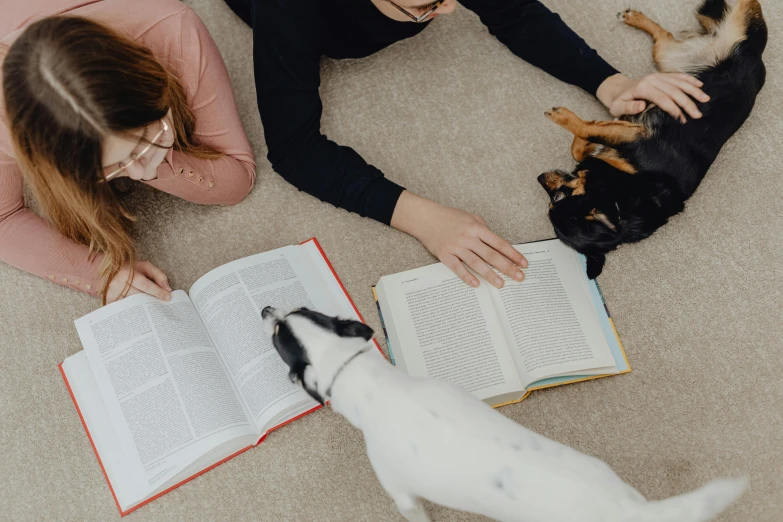 two woman reading books with dogs laying on the floor