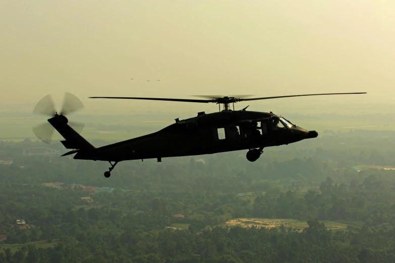 a military helicopter is flying above the trees