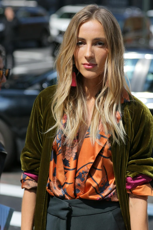 a blonde woman wearing an orange top and green jacket